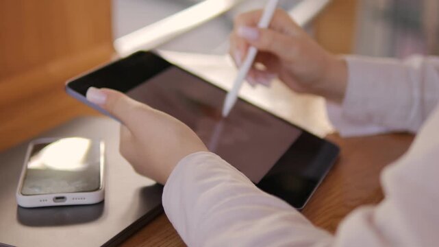 Woman is holding a tablet and a pen. A cell phone is on the table next to the tablet