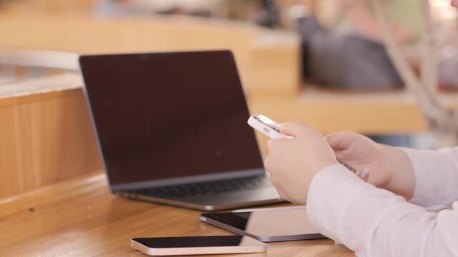 Person is using a cell phone and laptop on a table. The laptop is open and the cell phone is in the person's hand