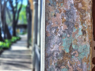 Close up of a wall surface showing many worn layers of rendering and paint, with a footpath in the background.