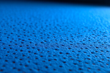 Close-up image of a textured blue surface with small, evenly spaced holes, highlighting the material's porous and breathable characteristics