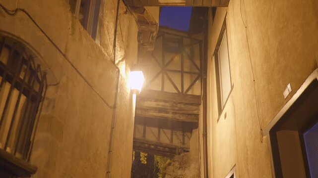 Narrow alleyway in Foix old town illuminated by streetlights at night, historic architecture and rustic atmosphere.