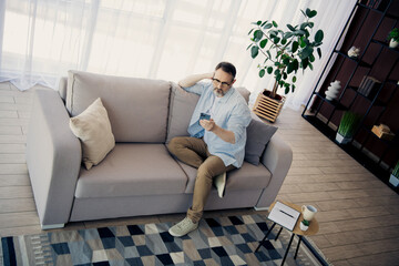 Mature businessman using a smartphone while sitting comfortably on a modern couch in a stylish and cozy living space