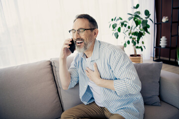 Mature man sitting on a couch talking happily on a smartphone, expressing joy and connection in a calm home setting