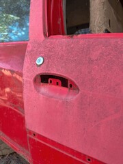 Red car door panel with missing handle, covered in dust and dirt, industrial junkyard scene, automotive mechanical structure, vintage corrosion texture, workshop engineering composition background.