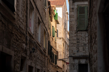 Fototapeta premium Sunlit stone alley with green shutters