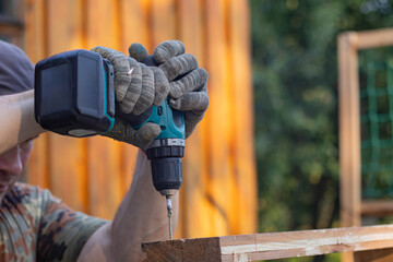 A man wearing gloves uses an electric screwdriver to tighten a screw.
