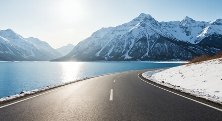 Winter road by mountain lake with scenic snowy peaks and bright sunlight