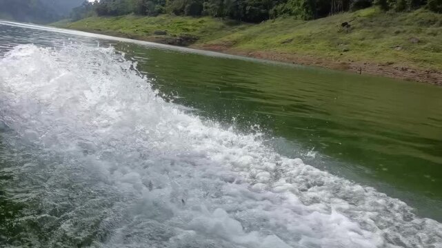 Boat wake green lake with foamy splash and grassy riverbank hillside shore rushing past cloudy sky evoking peaceful motion adventure and refreshing