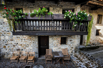 Wooden balcony with flowers on the facade of an old stone house in an ancient Italian village. Santa Margherita del Gruagno, Moruzzo, Udine province, Friuli Venezia Giulia, Italy.
