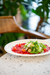 Gourmet beef carpaccio with arugula, cherry tomatoes, capers, and Parmesan on a plate. Elegant raw meat dish served on a stone table in a fresh, natural dining setting