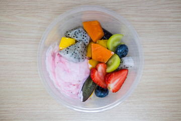 Strawberry greek yogurt topping with tropical fruit served in plastic bowl