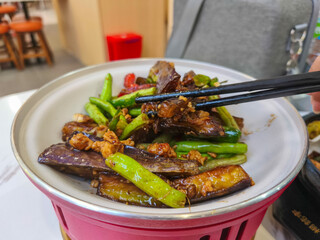 Delicious homemade stir fried eggplant with minced chicken and green beans, a popular Asian dish, served in a white bowl with chopsticks.