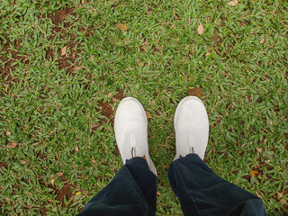 photo from above of plain white shoes and feet of an Asian man on green grass