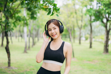 Happy young woman listening to music with headphones in a green park after workout, wearing sportswear. Concept of relaxation, healthy lifestyle, fitness, and positive energy in nature.