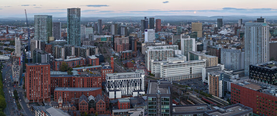 Panoramic aerial view of Manchester city skyline at dusk with a full Moon rising on the horizon.