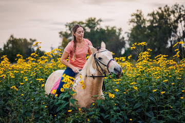 Woman riding horse in flowers meadow during sunset. Female rider enjoying recreational horseback riding in nature