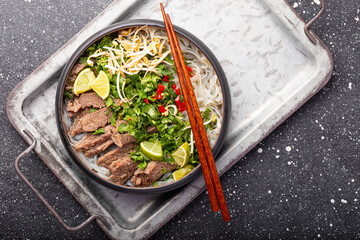 Pho Bo Vietnamese soup, bowl of fresh asian soup with rice noodle, beef meat, herbs, soy sprouts and chili on grey background, top view. Asian cuisine, comfort food.