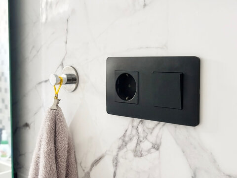 Modern black electrical outlet and switch mounted on elegant marble wall, accompanied by a soft towel hanging on a stylish hook, enhancing contemporary bathroom design
