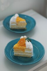 Close-up of a delicious homemade orange cake topped with whipped cream, orange glaze, and fresh tangerine slice on white background with a cake slice on a blue plate .