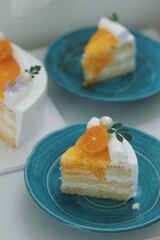 Close-up of a delicious homemade orange cake topped with whipped cream, orange glaze, and fresh tangerine slice on white background with a cake slice on a blue plate .