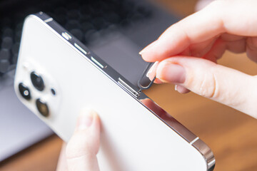 Woman's hand carefully inserts a SIM ejector tool into a modern smartphone to open the card slot,...