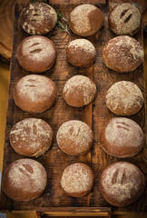 Rustic artisan bread rolls arranged in a wicker basket and on a wooden board, surrounded by wheat ears and burlap fabric, representing traditional handmade bakery and natural food craftsmanship.