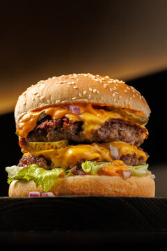 Close-up of a juicy double cheeseburger with melted cheese, lettuce, pickles, and onions on a sesame bun, captured on a dark background