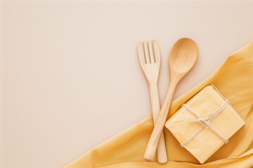 Neatly folded reusable beeswax wraps are displayed on a soft, warm surface alongside wooden utensils and a small wrapped package. Ideal for eco-friendly food storage
