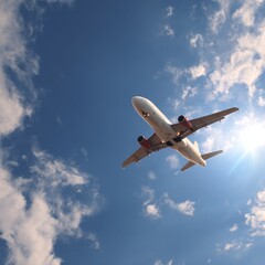 A passenger airplane soaring in the bright sky, captured from below, with fluffy clouds around