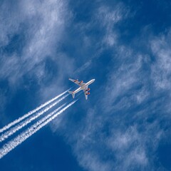 A plane soars through a blue sky leaving contrails behind. Witness the stunning interplay of aviation and atmosphere