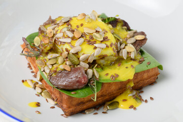 Salty waffle with poached egg, beef and sunflower seeds in sauce close-up