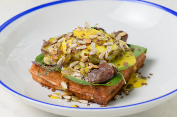 Salty waffle with poached egg, beef and sunflower seeds in sauce close-up