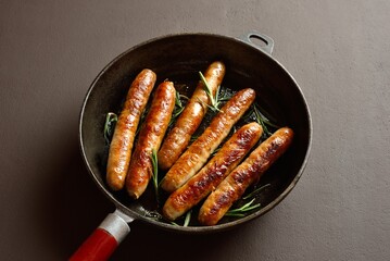 Delicious thin sausages in frying pan on dark background