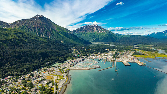 Aerial panorama of Seward harbor and Alaskan mountains. Panoramic aerial drone view of Seward harbor with boats, marina, and mountain range in Alaska under clear sky.