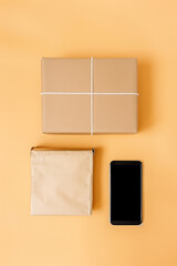A minimal flat lay displays a smartphone next to neatly wrapped packages on a vibrant orange surface. This setup illustrates convenience and modern online shopping trends