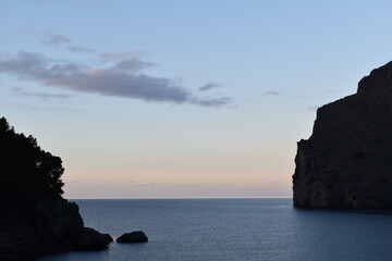 Coastal cliff at La Calobra in Mallorca, with the calm Mediterranean Sea and a soft pastel sunset sky creating a tranquil and picturesque seascape
