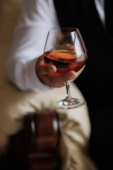 Person holding a glass of amber beverage in a cozy indoor setting during evening hours