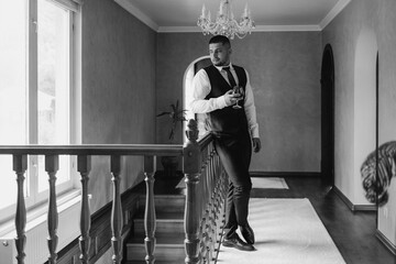 Man in formal attire enjoying a drink while standing on a staircase in an elegant home setting