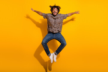 Obraz premium Energetic young man in a leopard print shirt jumping joyfully against a vibrant yellow background, showcasing a playful spirit