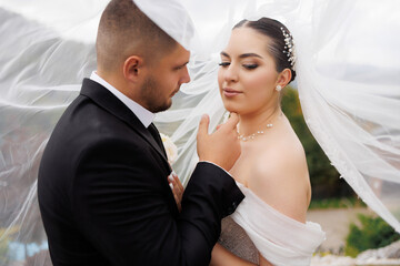Couple shares a romantic moment under wedding veil on a scenic outdoor terrace