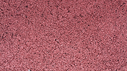 Title: Full frame close-up of a vibrant red or maroon colored athletic track or playground safety flooring made of rubber granules as a detailed texture or background.