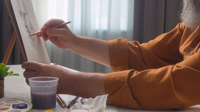 An elderly male artist drawing with pencils at home, focused and engaged in his creative process.