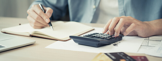 Deduction planning, debt asian accountant hand using calculator to calculating money balance from bill and income, cost budget expenses for pay money form personal individual on table at home.