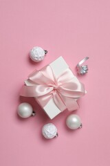 A white gift box with a pink ribbon with New Year's balls on color background, capturing the festive spirit of Christmas and New Year's.