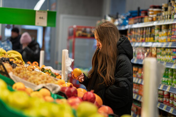 Cheerful teen girl shopping for organic fruits without plastic bags in local food store. Vegan zero waste girl choosing fresh fruits and vegetables in supermarket. Part of a series.