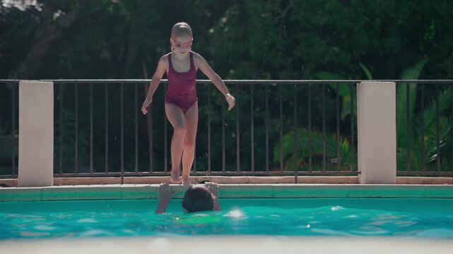 Young girl joyfully jumping into the swimming pool with water splashing in slow motion on a sunny day