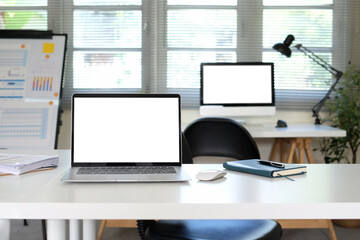 A laptop on a desk and a large computer monitor placed behind the laptop.