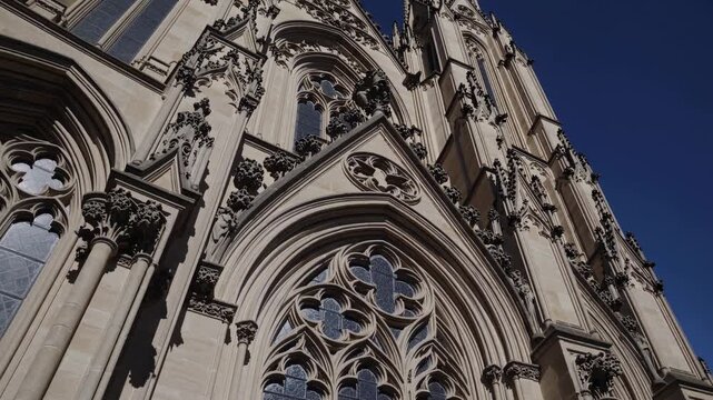 Dramatic low-angle video shot of a Gothic cathedral facade, highlighting intricate stonework against a clear blue sky.