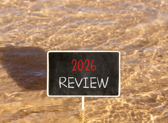 Naklejka premium 2026 Review symbol. Concept words 2026 Review on beautiful black blackboard. Beautiful Red sea water background. Business and 2026 review concept. Copy space.