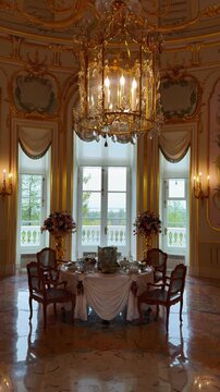 A vertical, medium-telephoto, indoor shot captures a lavish dining room or private chamber with a set table, illuminated by a glittering gold and crystal chandelier and bright natural light streaming